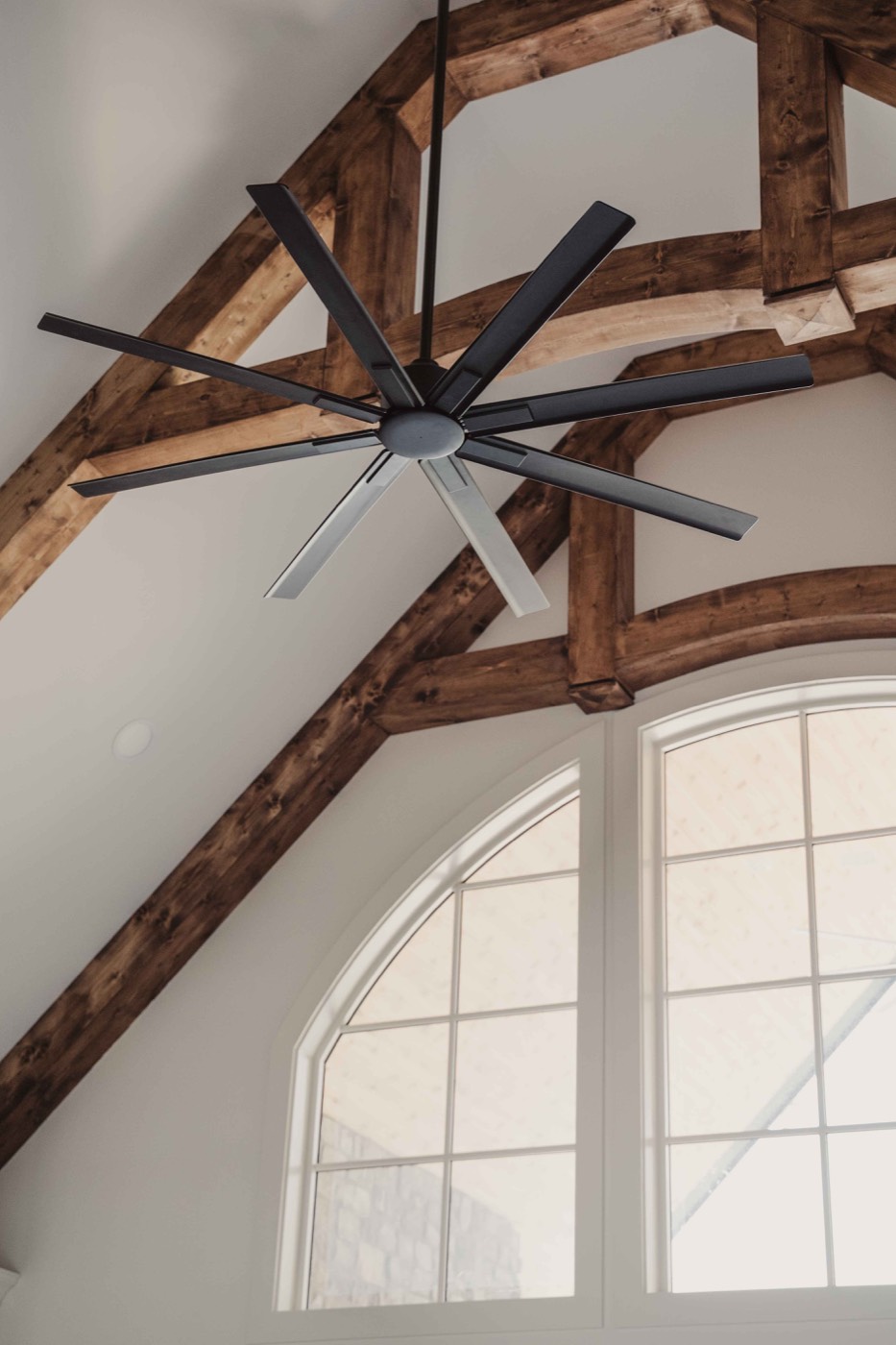 Close view of a black ceiling fan between timber trusses